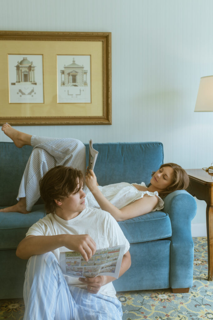 Bride and groom lounging on blue velvet couch reading newspaper, anniversary photoshoot