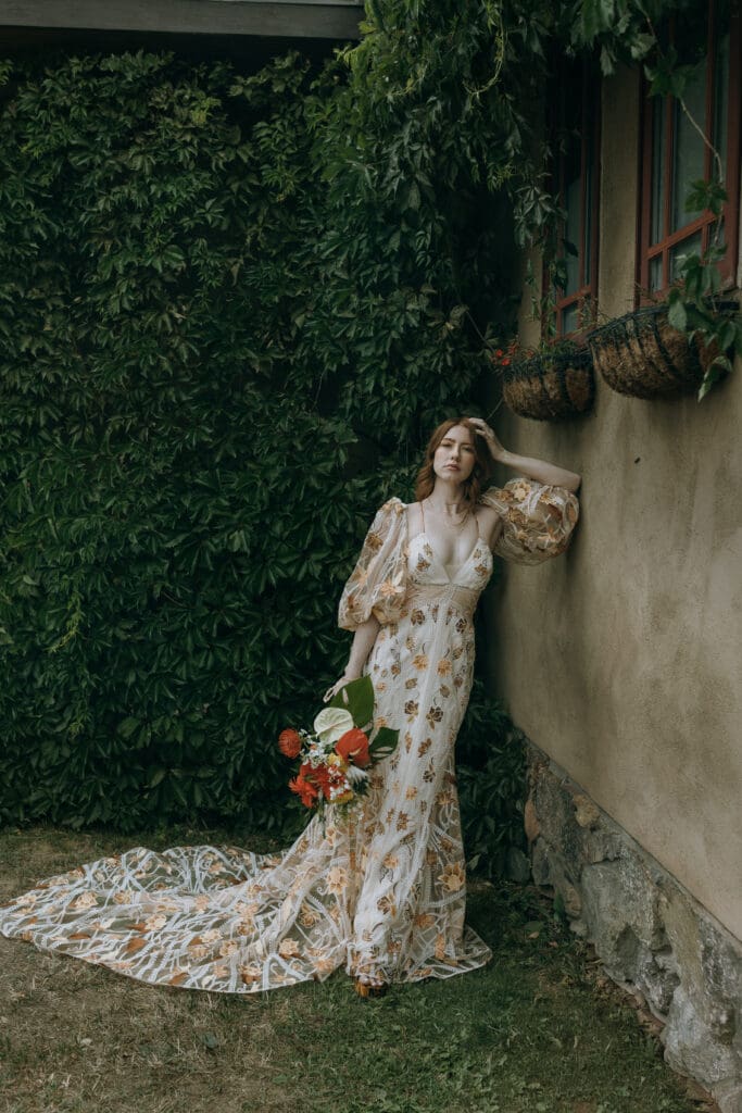 Bride in a floral Rue de Seine gown stands against a vine-covered wall at Ring Raven Ranch in Colorado